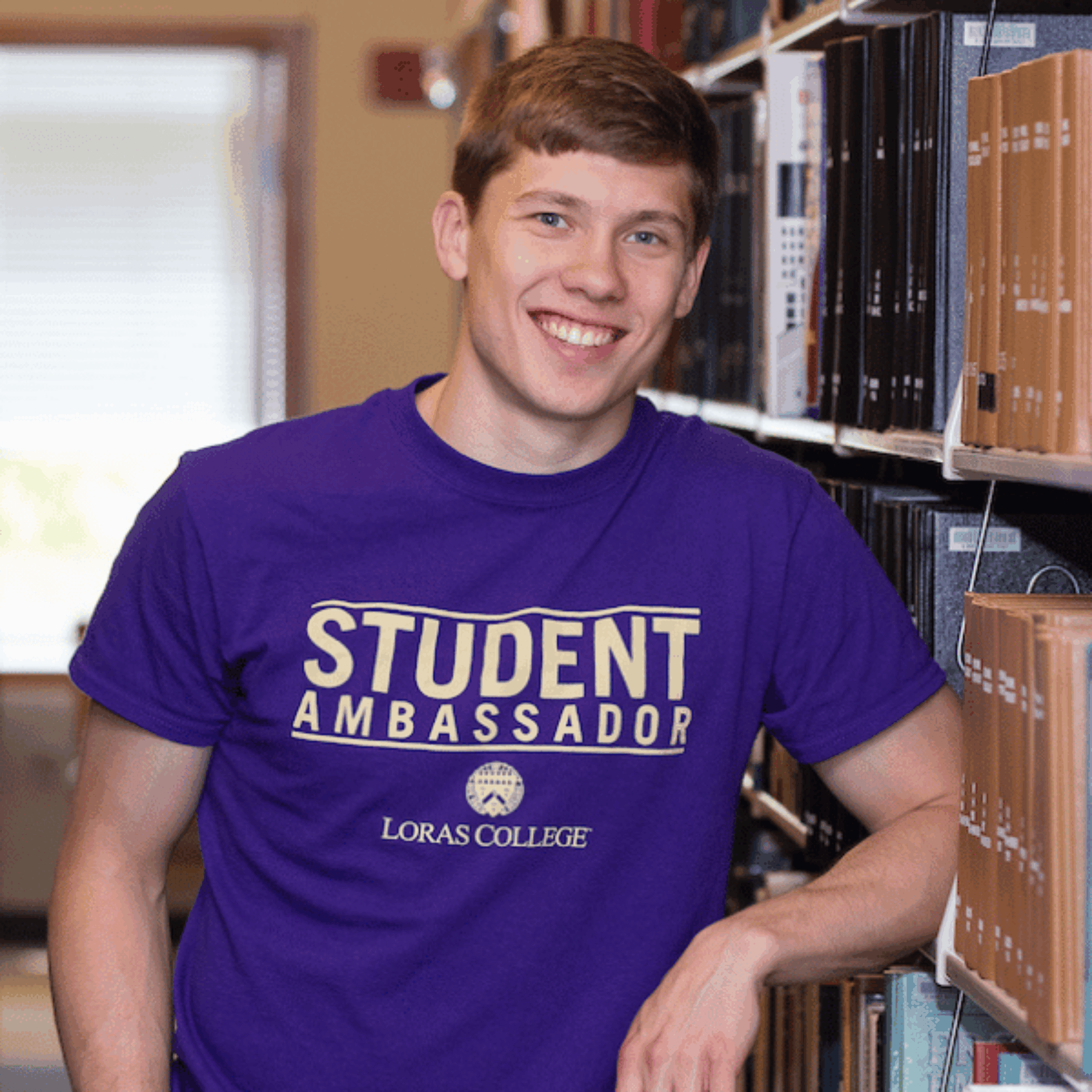 student standing by books in the library