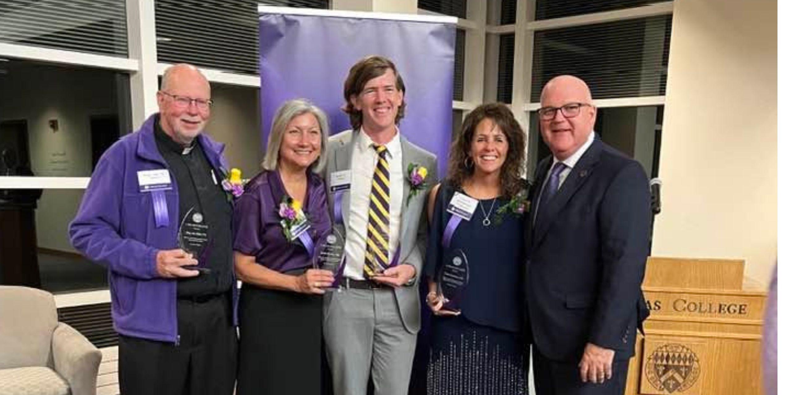 Five individuals holding glass award trophies