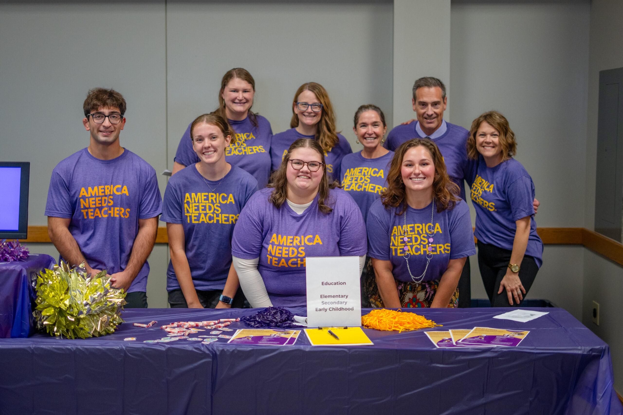Group of people wearing purple shirts with yellow writing "America Needs Teachers"