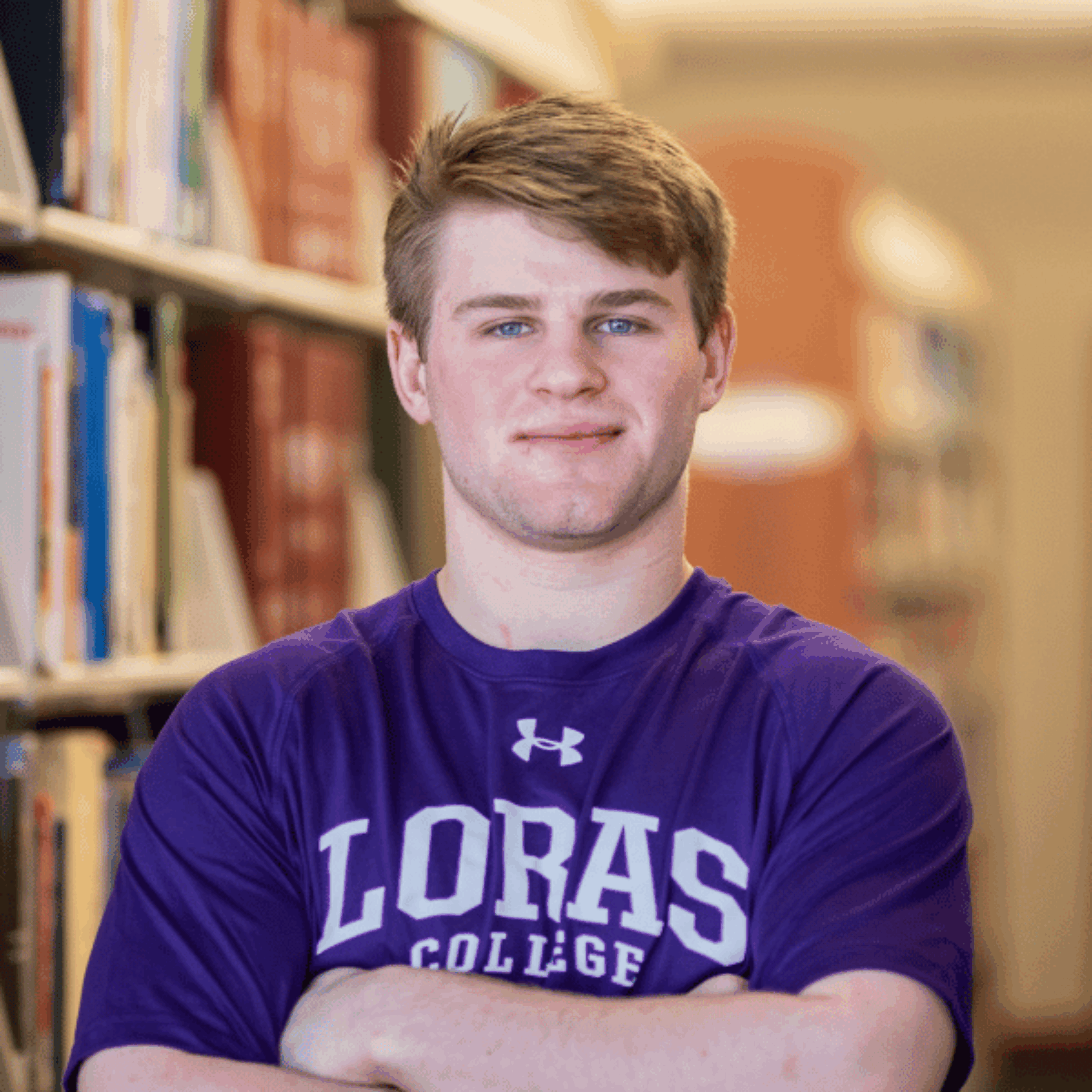 student standing by books in the library
