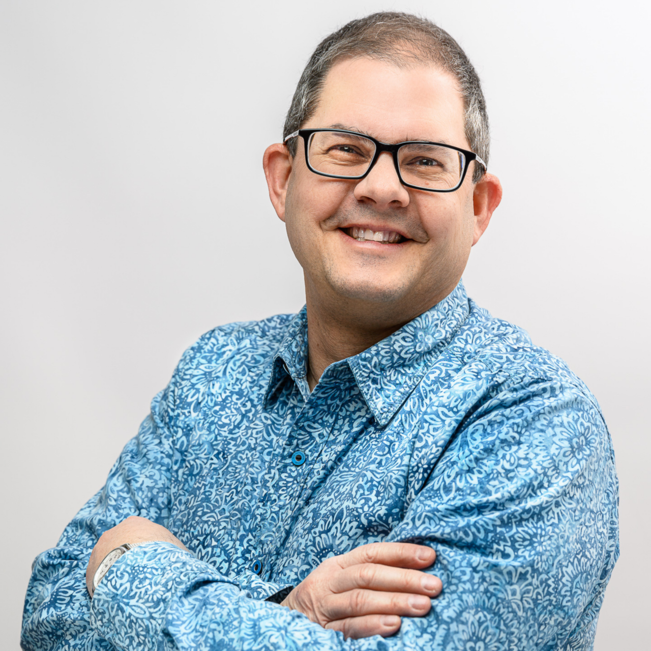 Smiling professor wearing glasses and a light blue, collared, dress shirt
