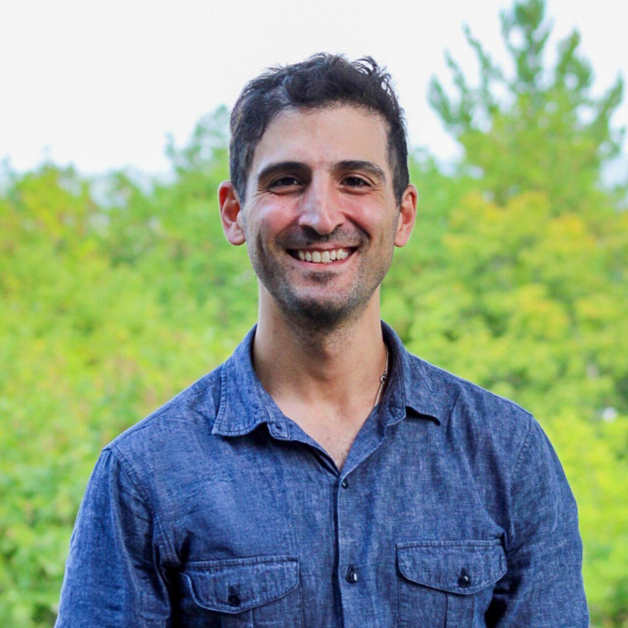 Employee wearing a blue shirt and standing in front of green trees