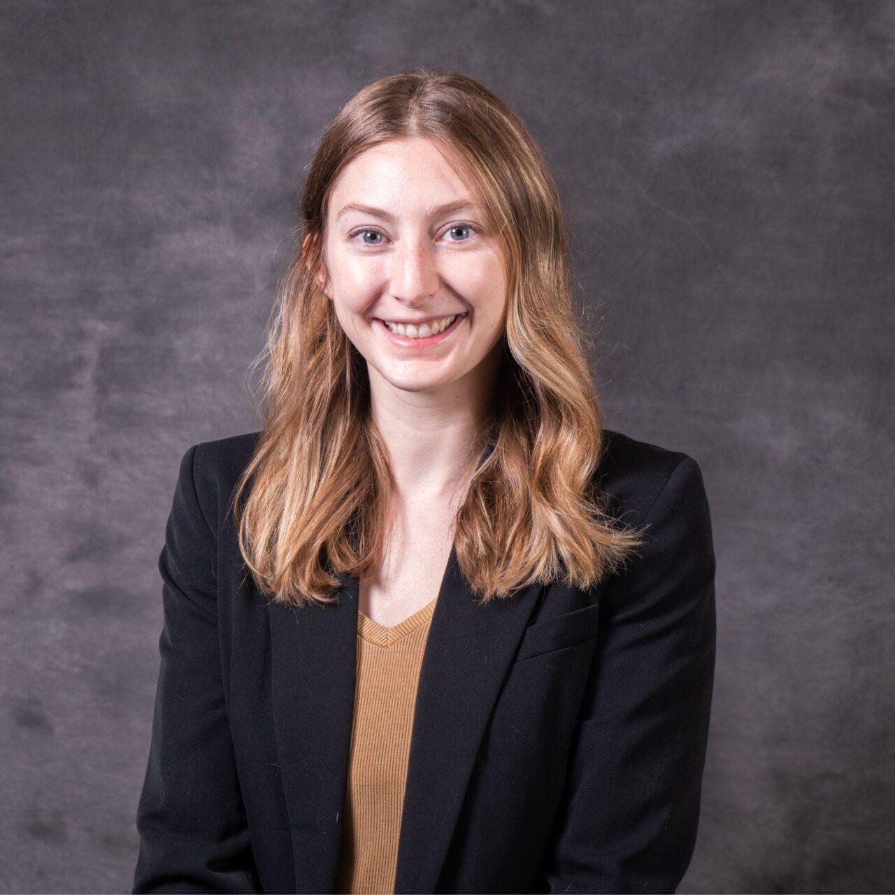 Employee smiling at the camera wearing a brown sweater and black blazer