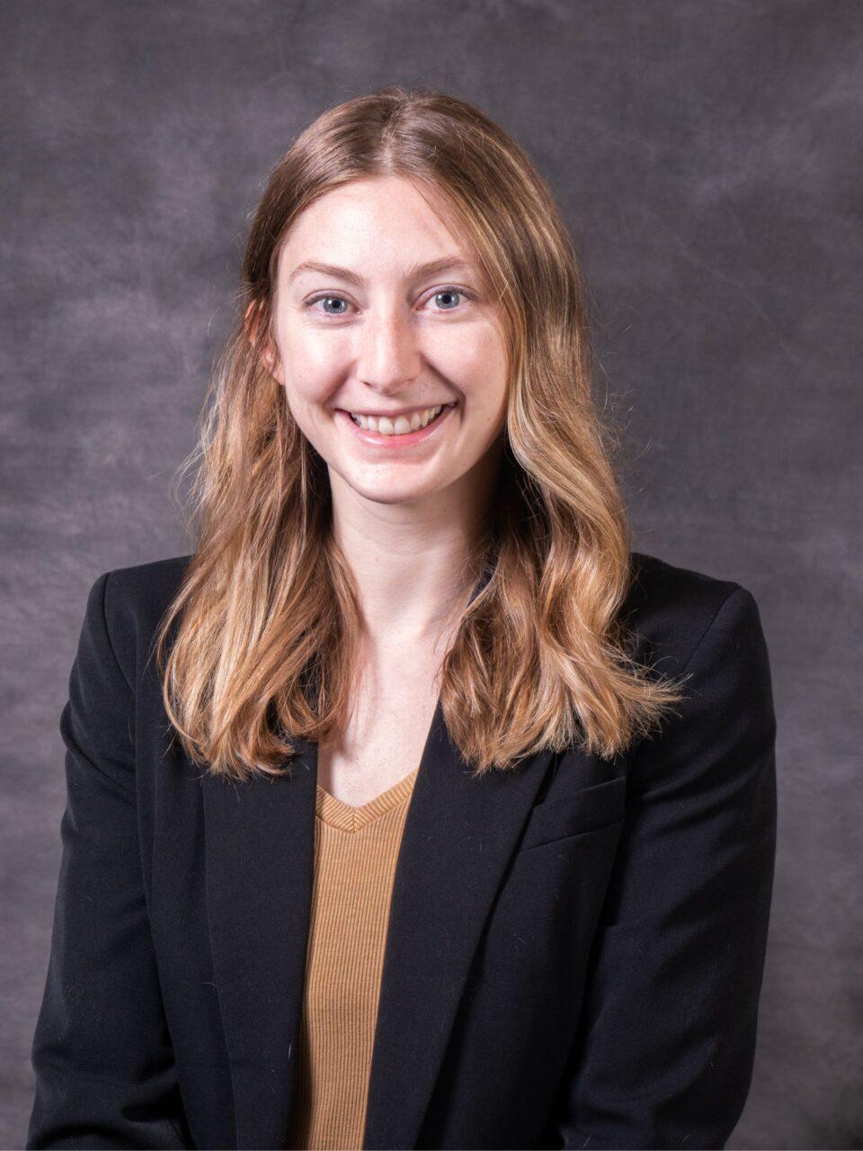 Employee smiling at the camera wearing a brown sweater and black blazer