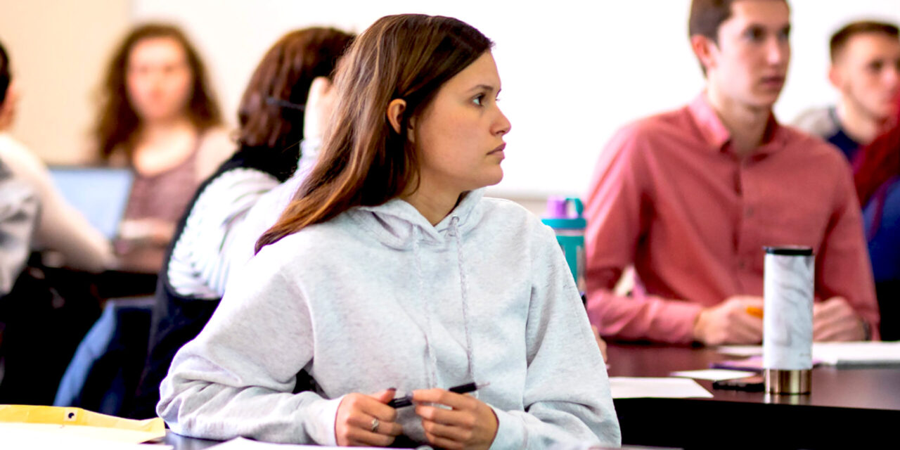Female student focused in classroom looking at Professor