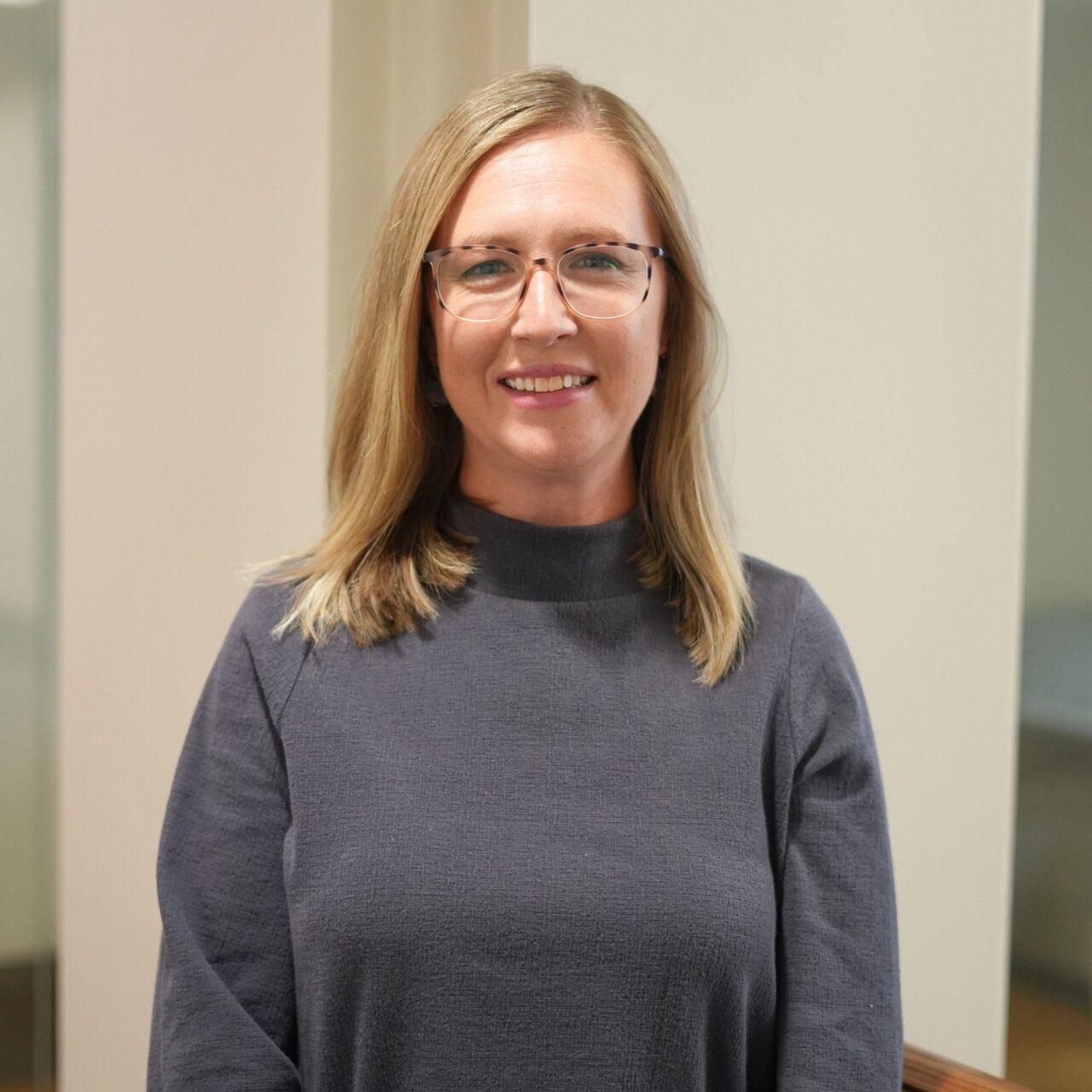 Employee smiling at the camera wearing a grey turtleneck and glasses