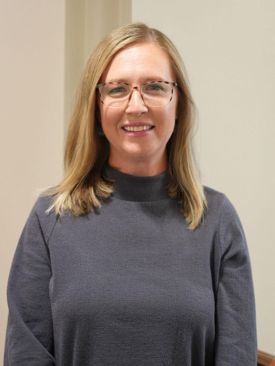 Employee smiling at the camera wearing a grey turtleneck and glasses