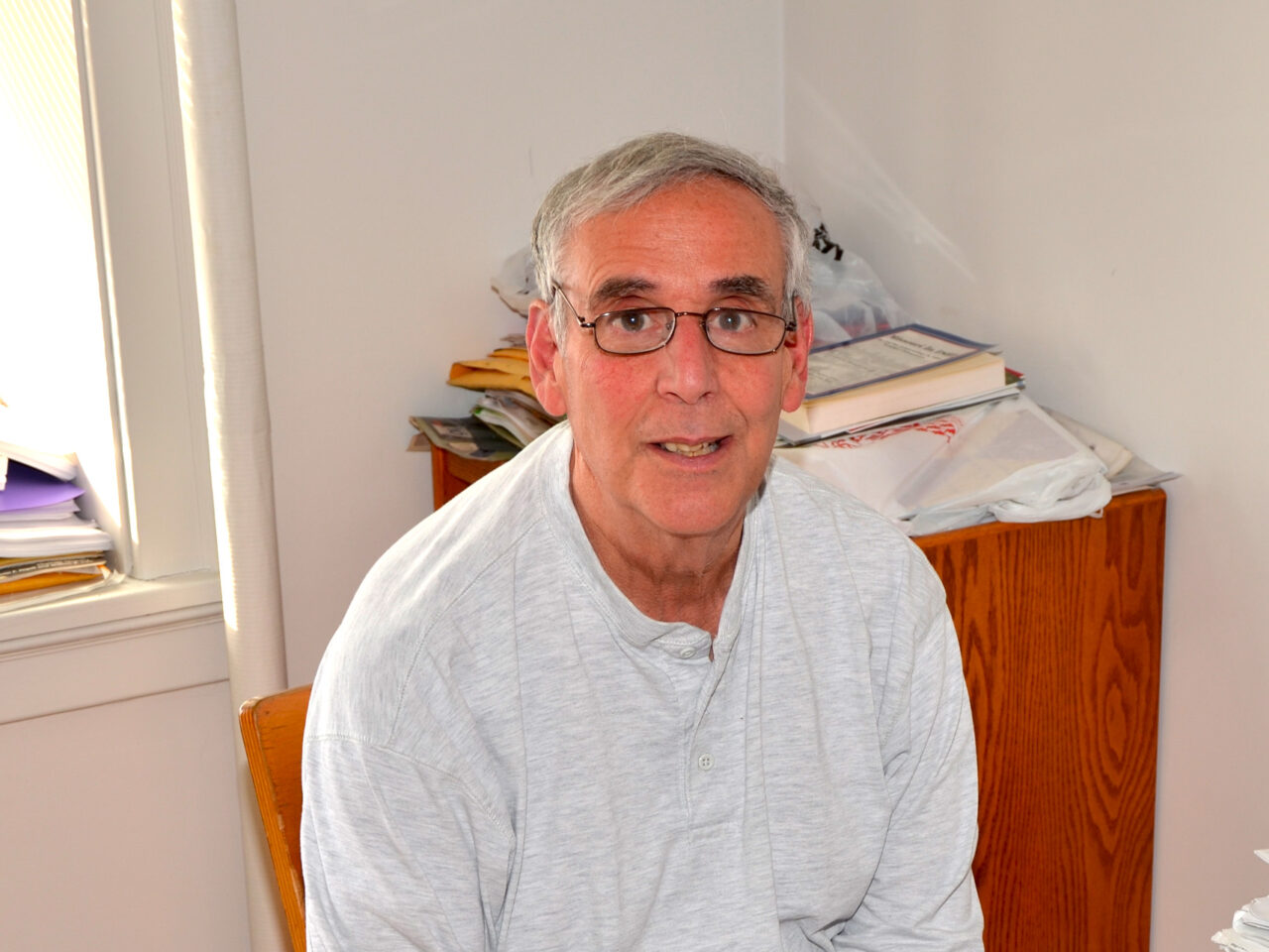 David Salvaterra, PhD, professor emerita is sitting at his desk in 2016 wearing a white sweater