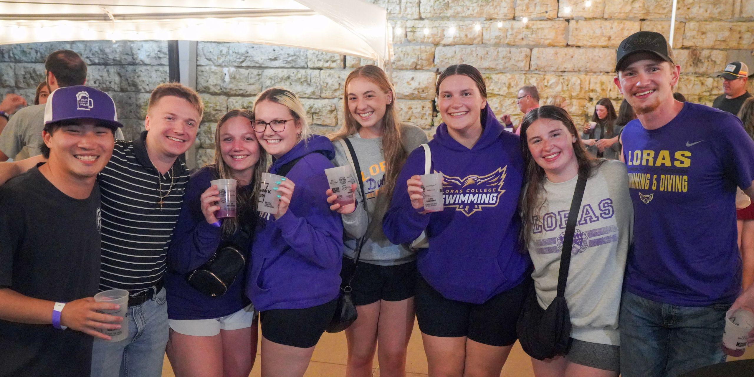 Eight people in purple and black holding cups up smiling