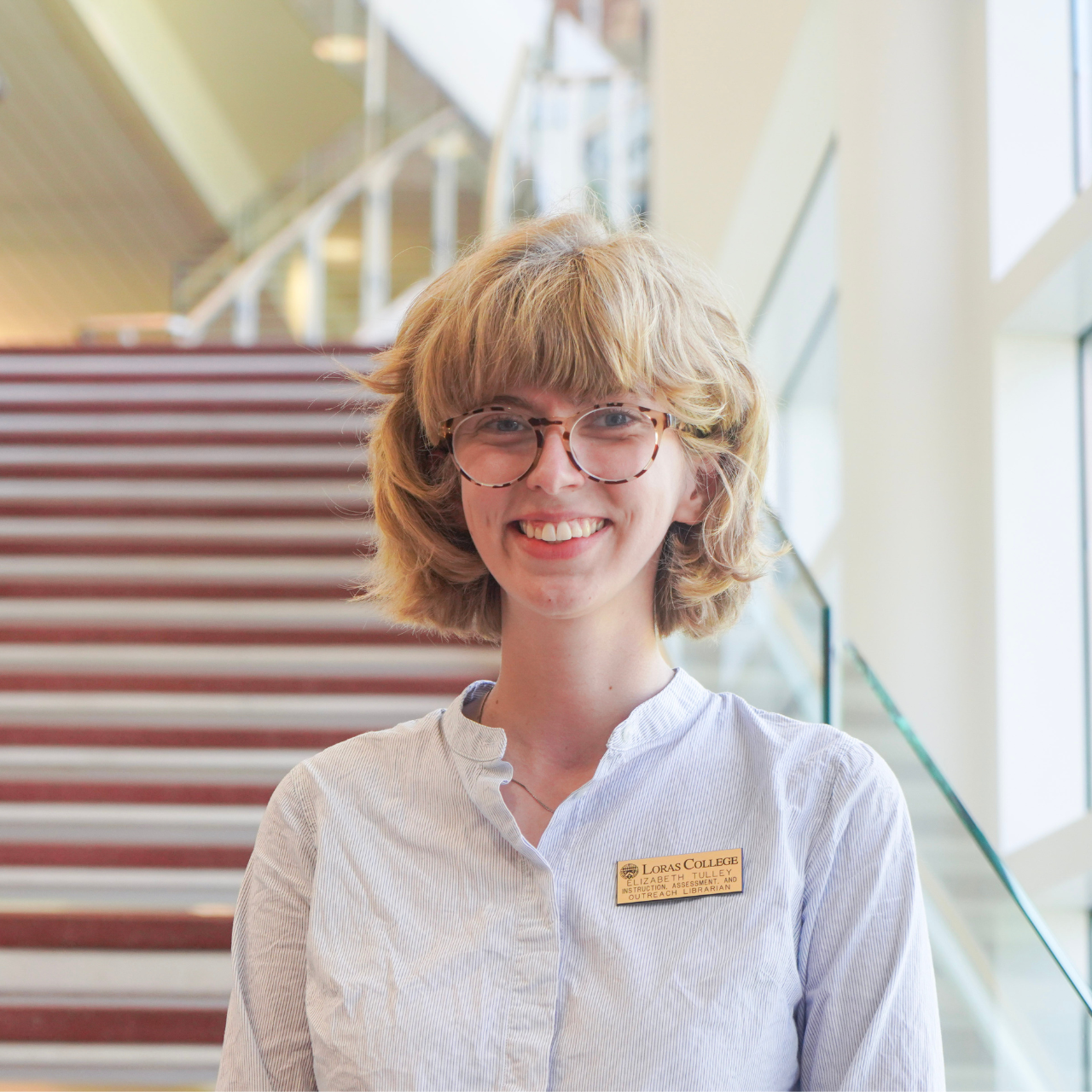 woman smiling at the camera in front of stairs and a bright window