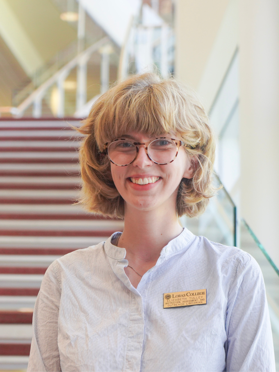 woman smiling at the camera in front of stairs and a bright window