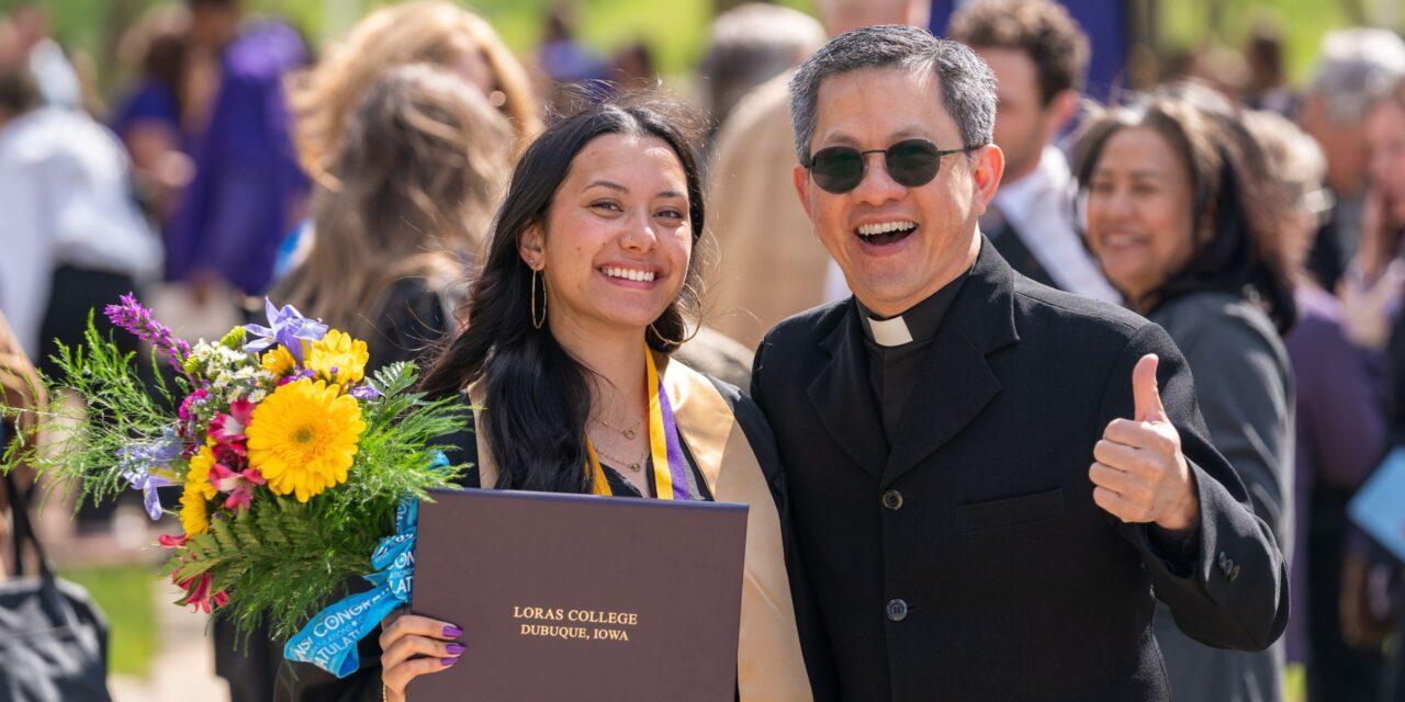 Graduate celebrating with flowers and campus priest