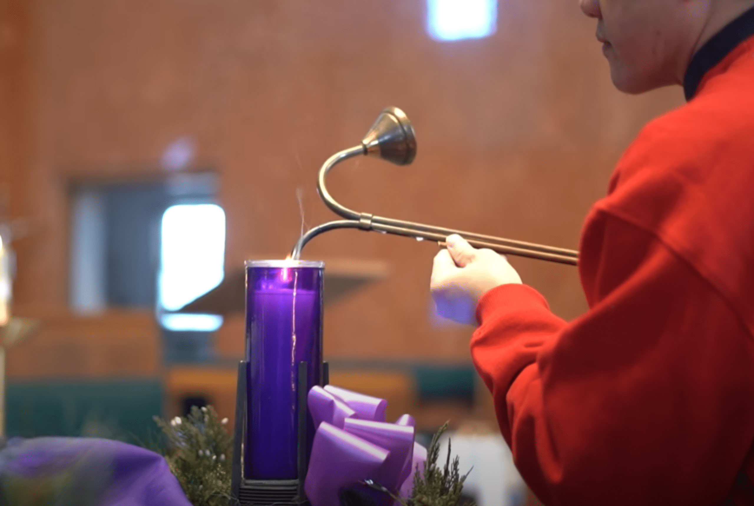 person in red sweater lighting purple candle on fire