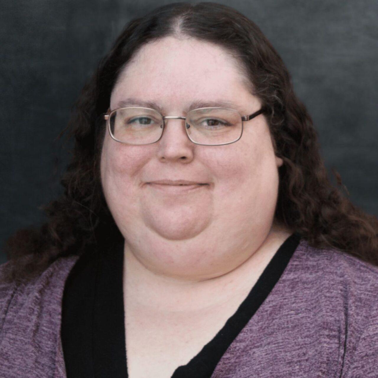 smiling Loras employee with purple shirt and long hair with glasses