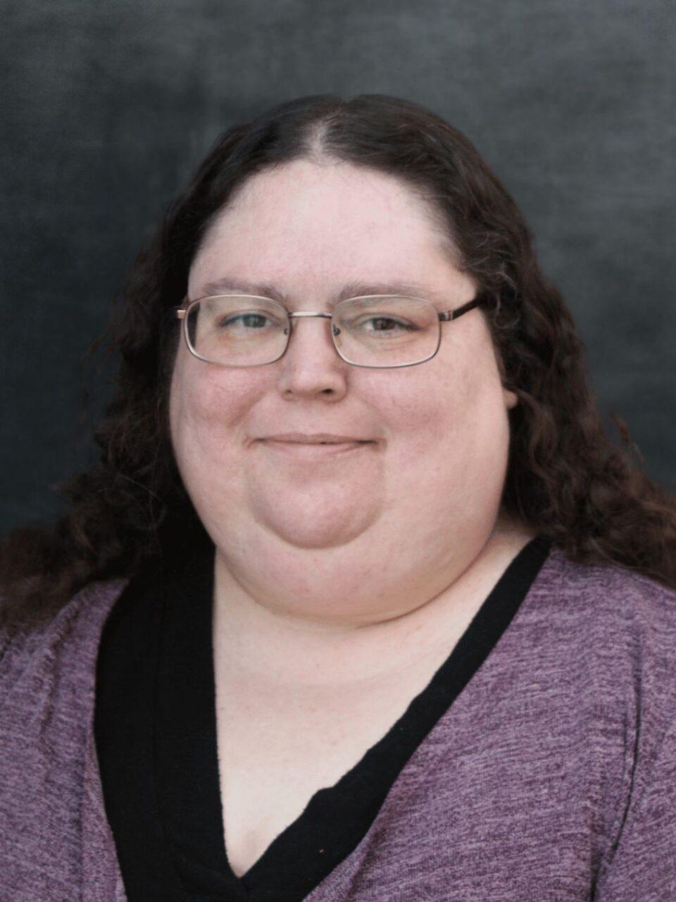 smiling Loras employee with purple shirt and long hair with glasses