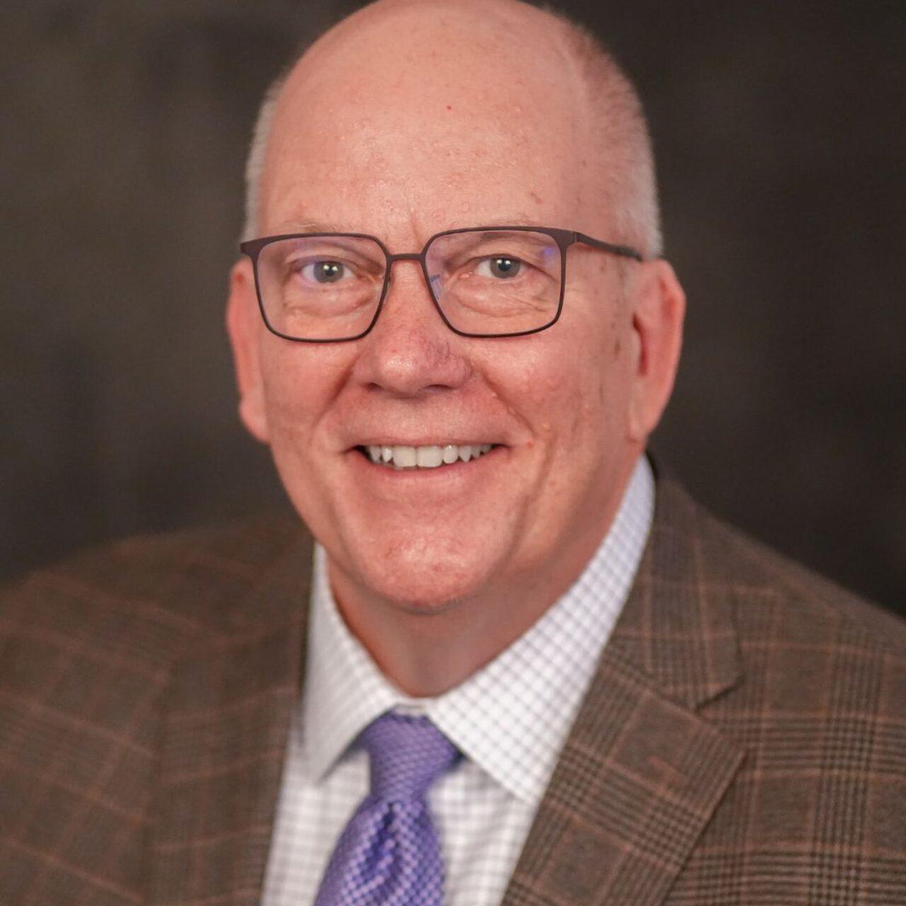 smiling adult in white button down shirtsmiling adult in white button down shirt, purple tie, and brown suitcoat