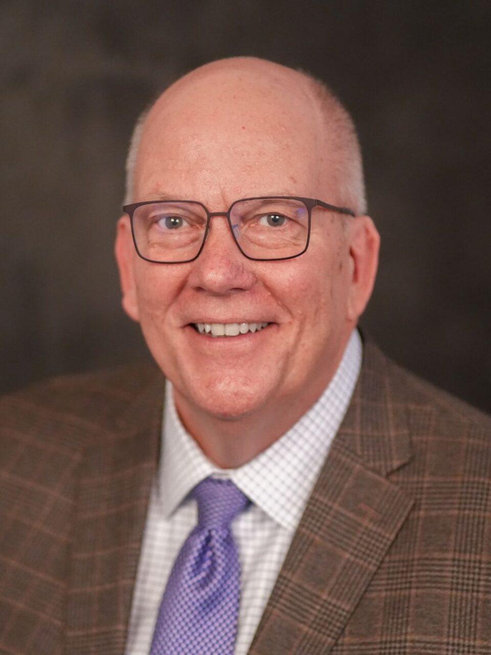 smiling adult in white button down shirtsmiling adult in white button down shirt, purple tie, and brown suitcoat