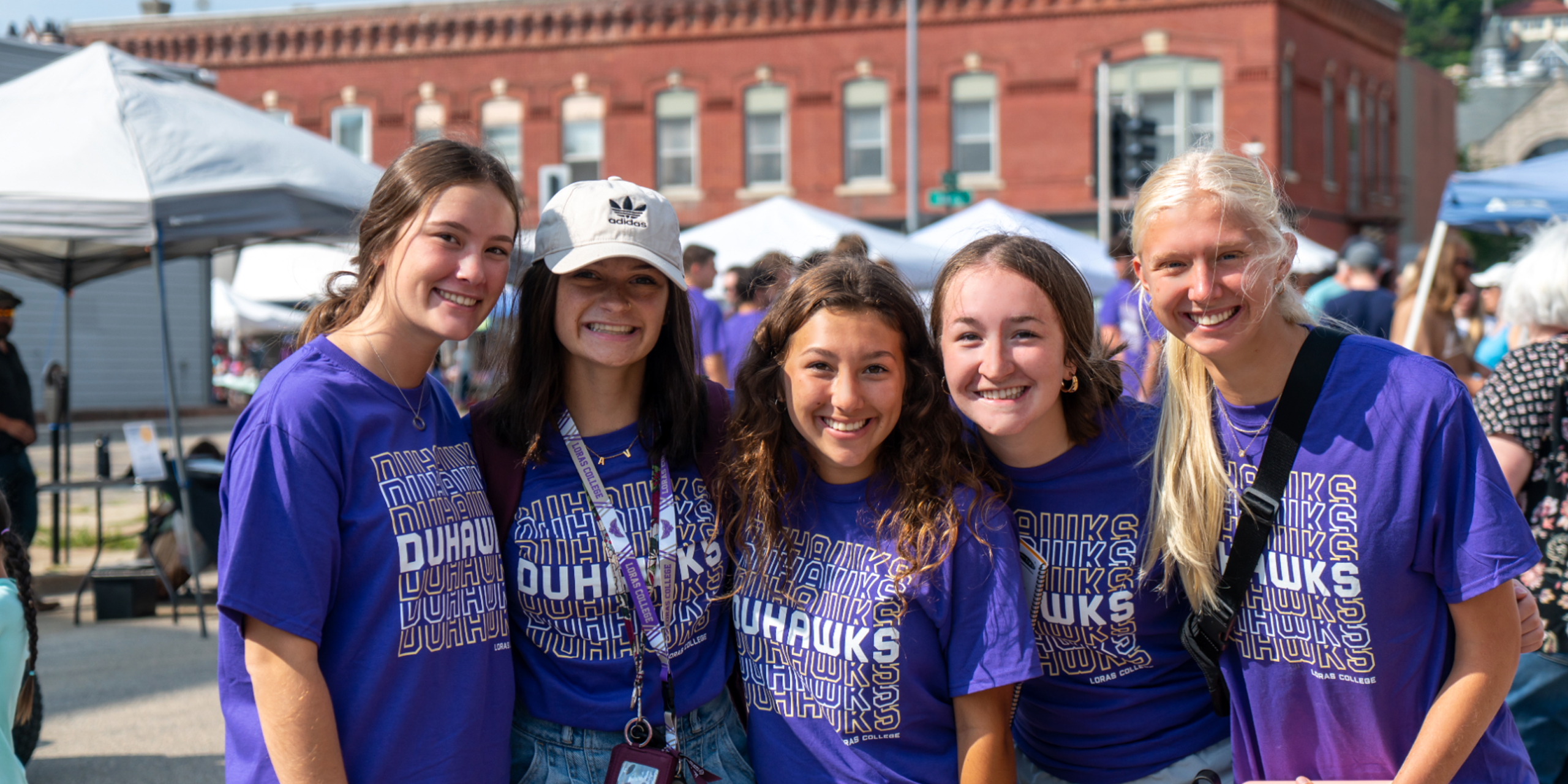 group of five female students in purple t-shirts at farmers market outside