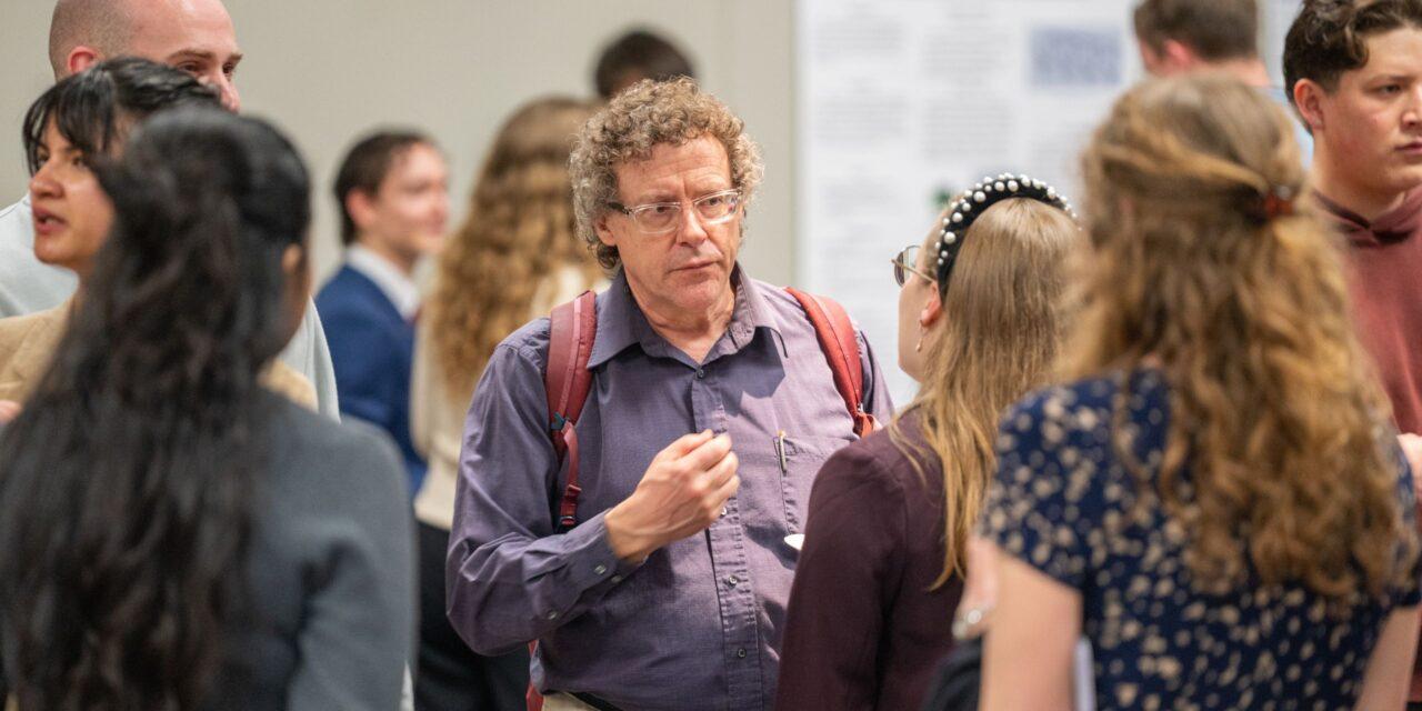 Man wearing purple shirt looking intently and talking with student
