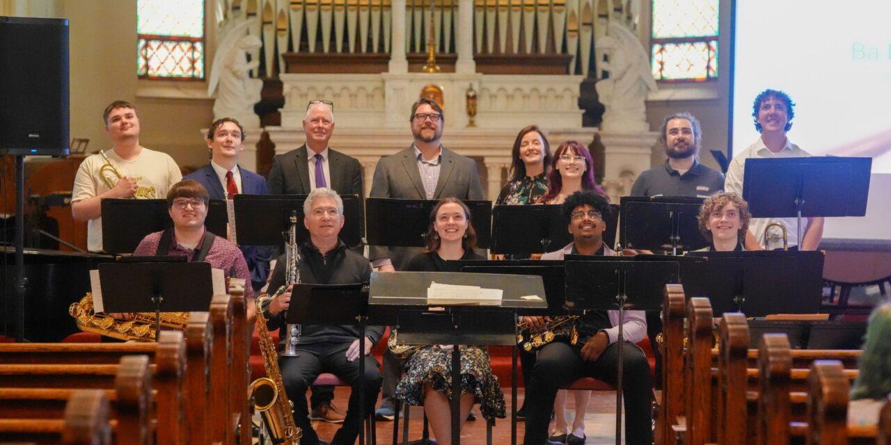 two rows of musicians smiling and posing with instruments in a chapel