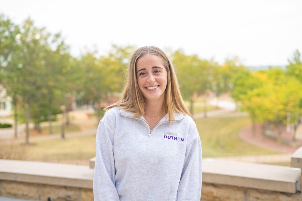 smiling student standing outside with fall colored trees in the background
