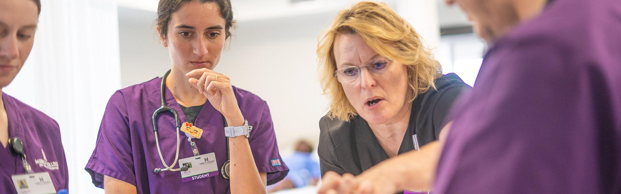 group of nursing students watching female faculty pointing something out.