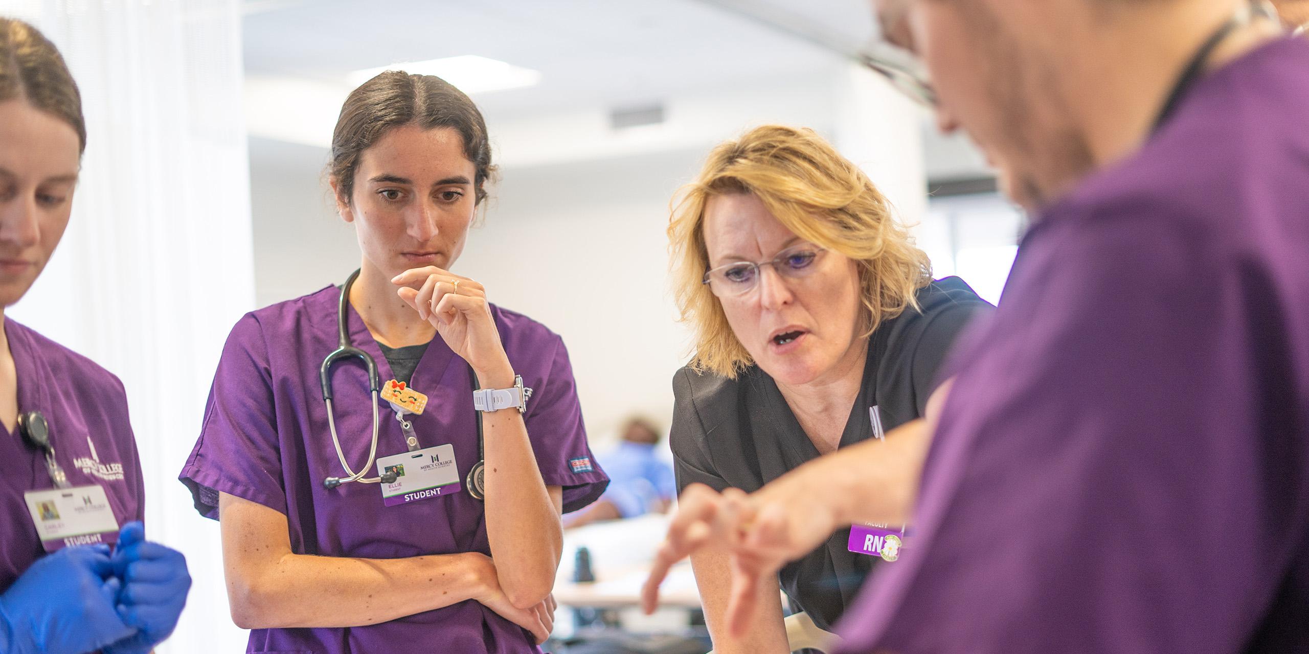 group of nursing students watching female faculty pointing something out.