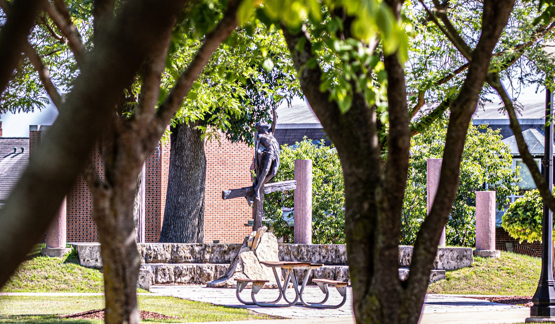 Jesus Statue on the lawn with picnic table in front, viewed through trees