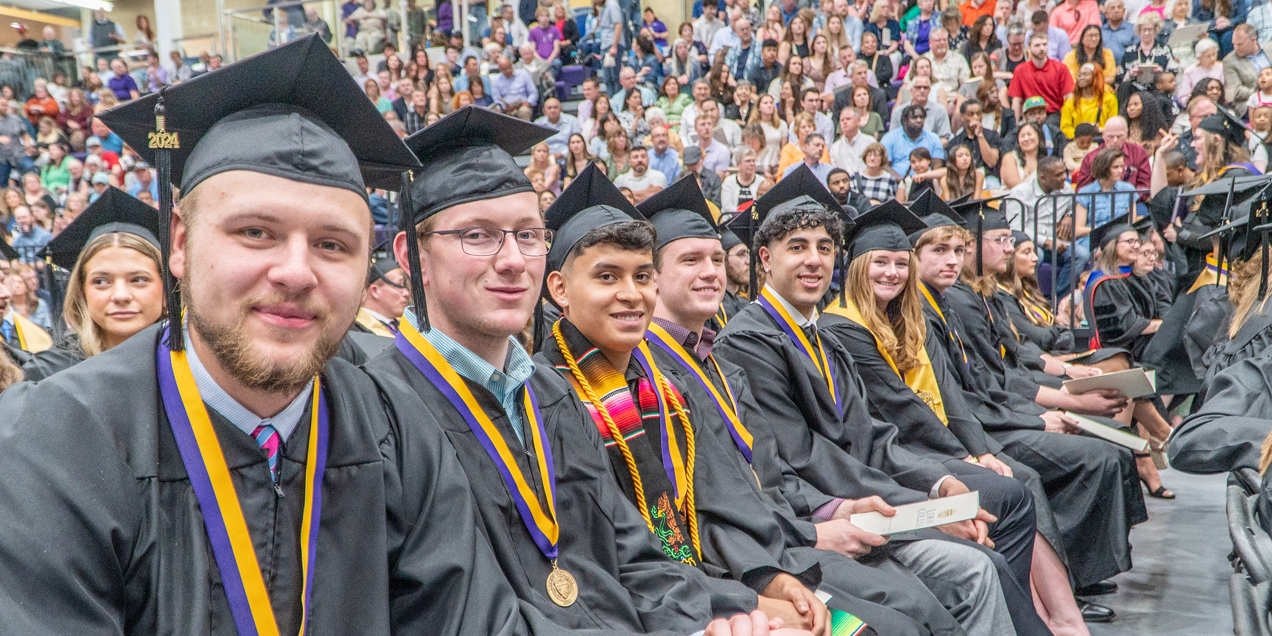 students in cap and gowns in row smiling at camera during graduation ceremony