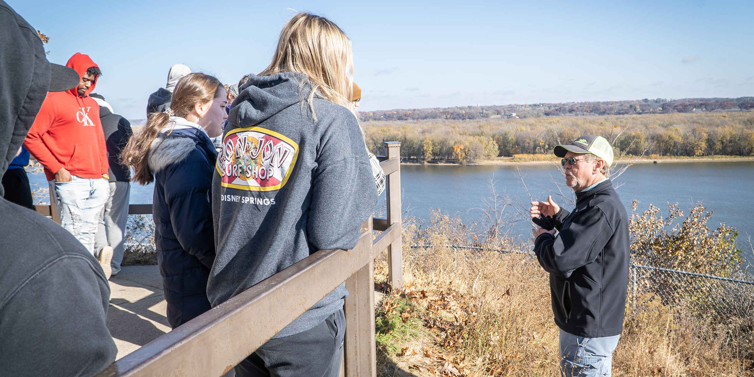 male teacher speaking to students outside in nature on bluff overlooking a river