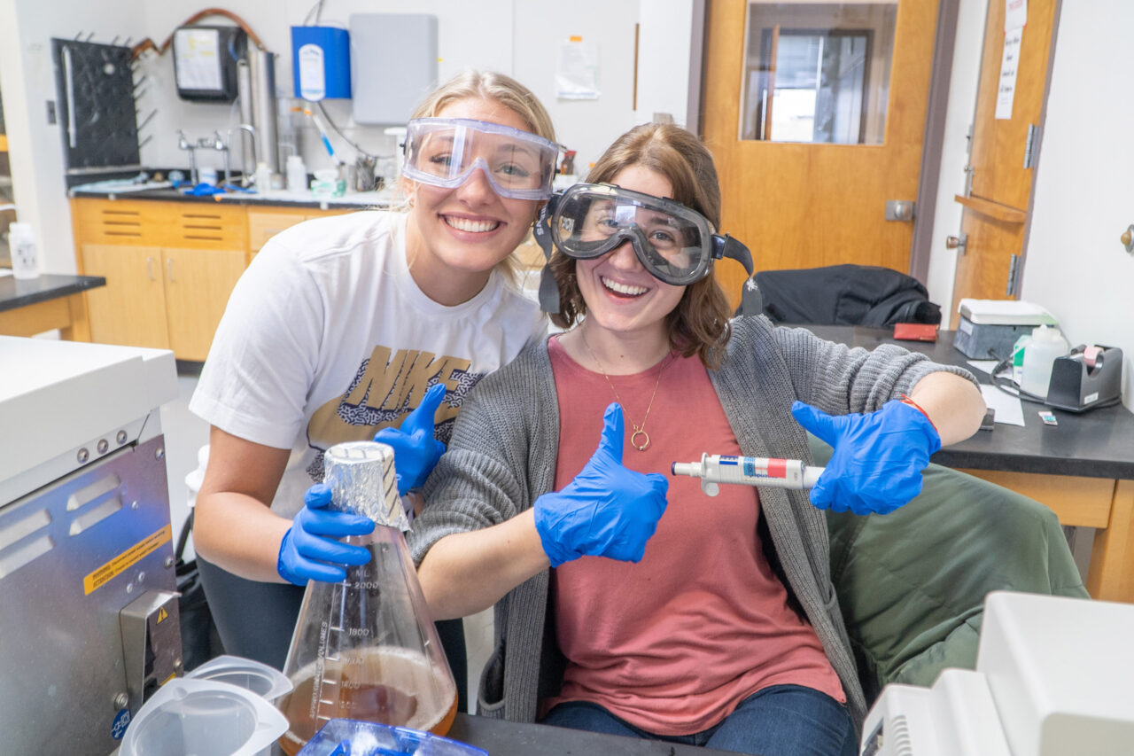 Two students smiling with lab equipment
