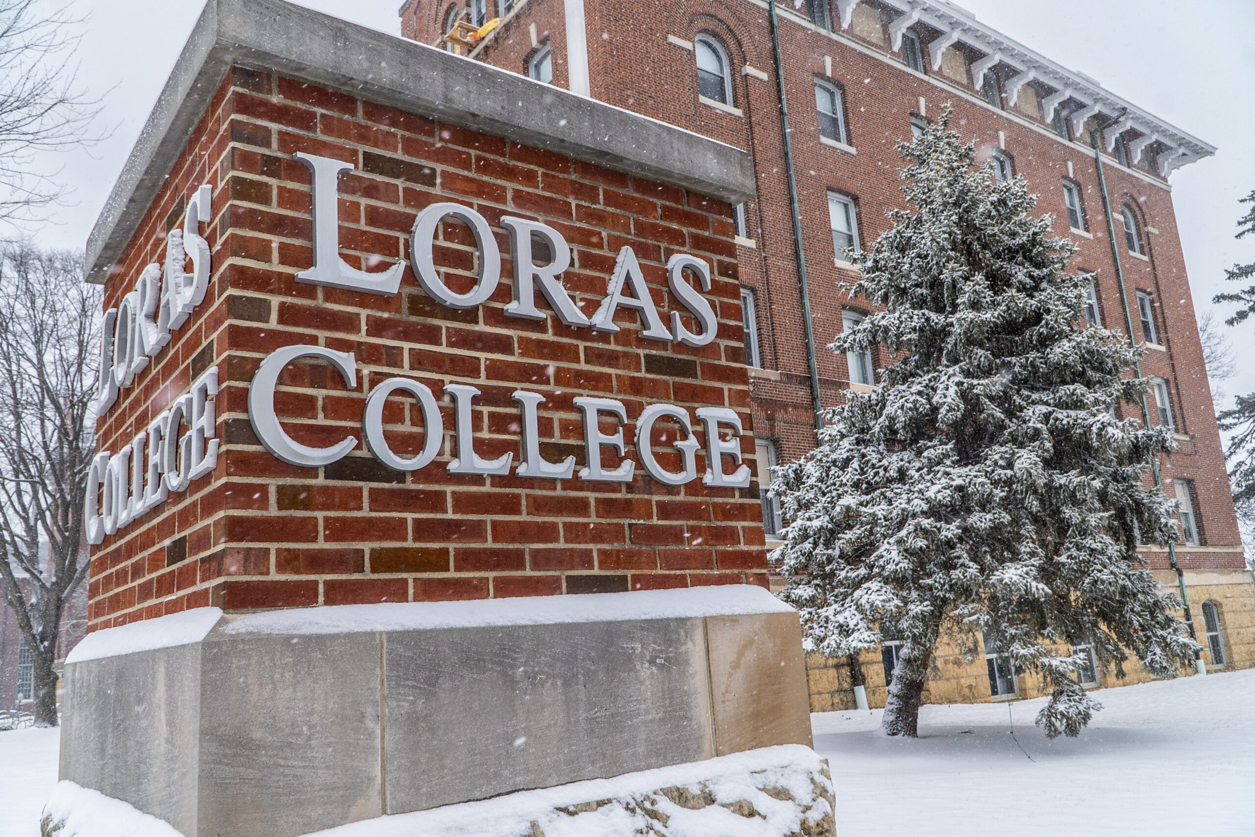 Loras College brick piker in front of Keane Hall with large trees