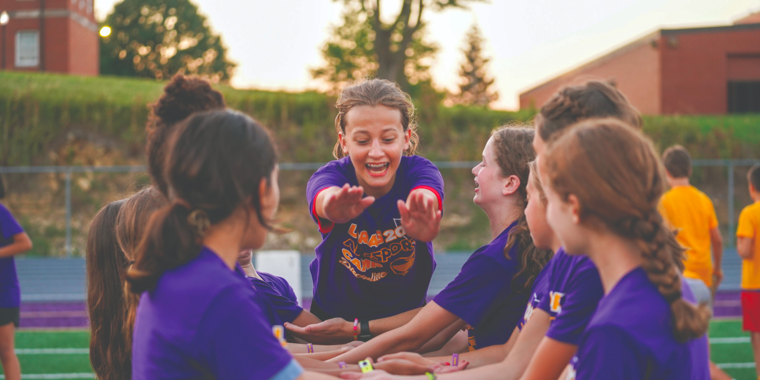 All-Sports Camp student smiling and diving into the arms of her teammates who are waiting to catch her.